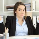 Woman sitting at a desk shrugs.