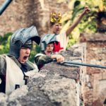 Three boys dressed as knights wield swords as they defend their castle wall.