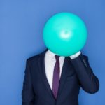 A business person holds a big balloon in front of their face.