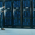 Two IT professionals walk along a wall of mainframes in a data centre discussing various things