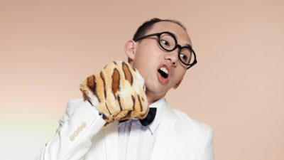 A man in a tuxedo punches himself on the chin with a tiger puppet.