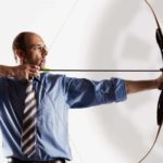 Business executive aiming bow and arrow at target.