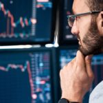 An ASX 200 market analyst holds his hand to his chin and looks closely at his computer screens watching share price movements