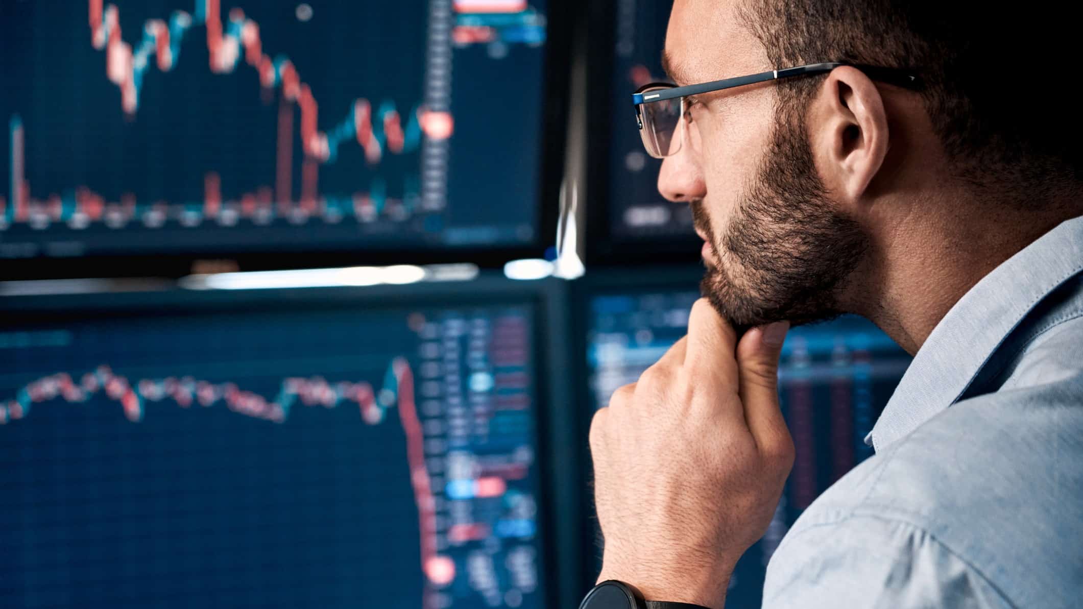 An ASX200 market analyst holds his hand to his chin and looks closely at his computer screens watching share price movements