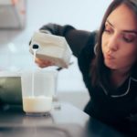 A woman is unsure as she pours milk into a glass, has it gone sour?