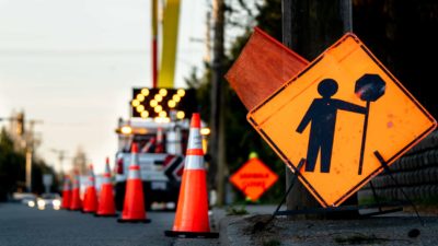 A street is filled with roadwork signs, flashing arrows and orange cones, causing traffic to slow.