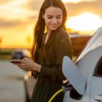 A woman smiles as she powers up her electric car using a fast charger.