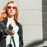 a woman holds out an electric vehicle charger with a satisfied look on her face behind cool sunglasses.