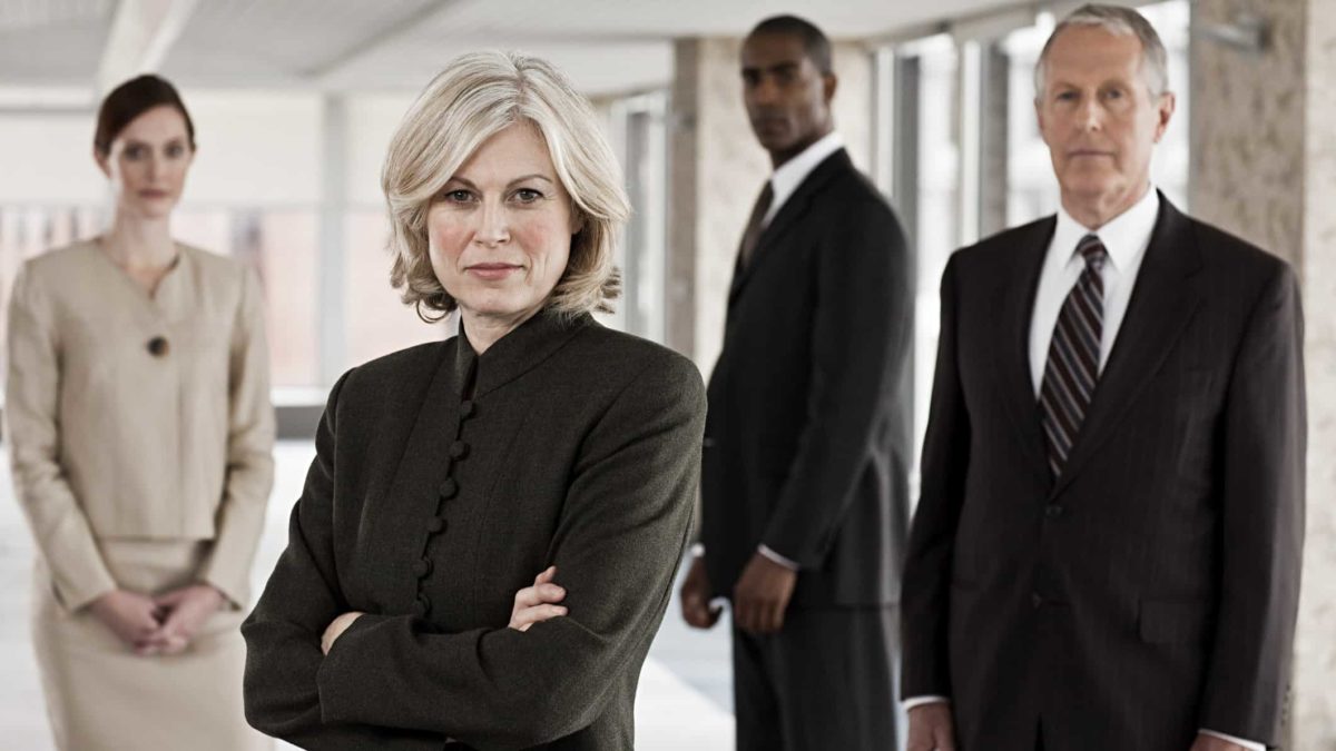 a panel of formidible business people stand in a group with serious looks on their faces as if in judgement of what's before them.