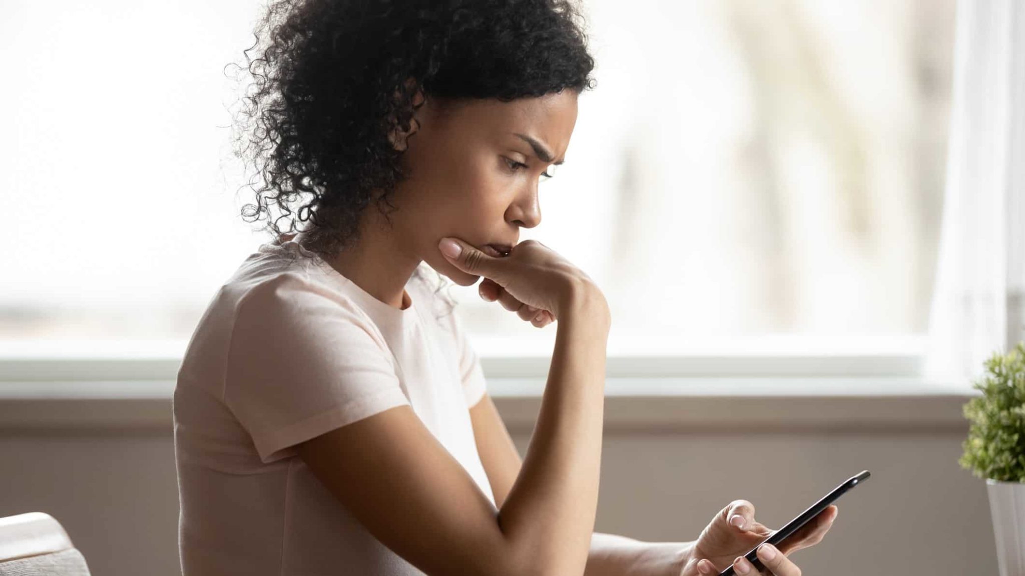 She is serious. Afro American woman holds smartphone. Black woman thinking.