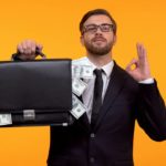 A man in suit and tie is smug about his suitcase bursting with cash.