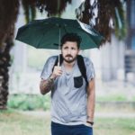 A man slumps his shoulders as he stands under his umbrella in the rain.