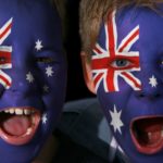 Two young boys with face painted in Australian flag cheer.