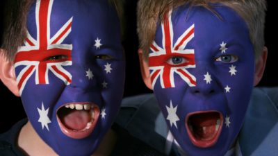 Two young boys with face painted in Australian flag cheer.