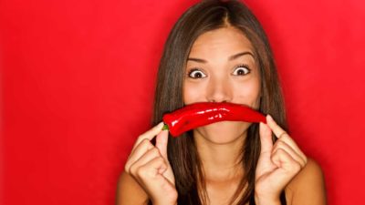 A woman holds a chilli in front of her mouth as an upside down smile.