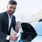 A man wearing a suit and holding an EV charger gives the thumbs up.