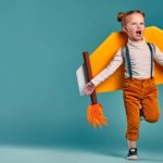 A little girl with red hair runs excitedly with a rocket strapped to her back, trying to launch.