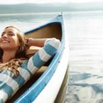 A woman lies back and relaxes in her boat with a big smile on her face as it floats on the rising tide.