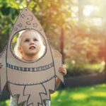 A little girls looks up longingly through a rocket she has made from cardboard, dreaming of shooting to the stars one day.