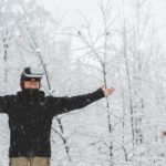 A person stands still with a virtual reality technology headset on and arms outstretched, surrounded by frozen ice and snow.