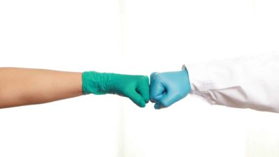 Two people wearing gloves giving each other a fist bump.