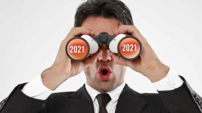 A man in a suit looks through binoculars with 2021 on them.