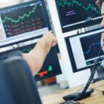 Two brokers analysing the share price with the woman pointing at the screen and man talking on a phone.