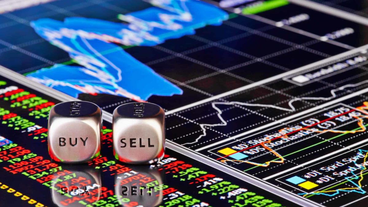 Buy and sell written on silver cubes on a stock market chart.