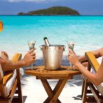 Beautiful holiday photo showing two deck chairs close-up with people sitting in them enjoying the bright blue ocean and island view while sipping champagne and enjoying the good life thanks to Pilbara Minerals share price gains in recent times