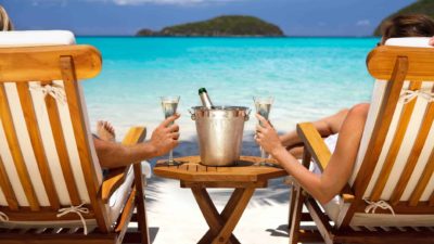 Beautiful holiday photo showing two deck chairs close-up with people sitting in them enjoying the bright blue ocean and island view while sipping champagne and enjoying the good life thanks to Pilbara Minerals share price gains in recent times