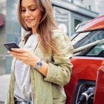 Happy woman on her phone while her electric vehicle charges.