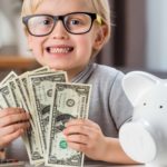 Kid holding banks notes alongside a whit piggybank, symbolising dividends.