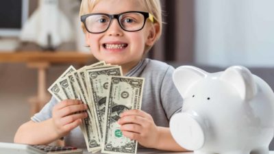 Kid holding banks notes alongside a whit piggybank, symbolising dividends.