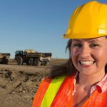 Female South32 miner smiling with mining machinery in the background.