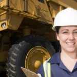 Female miner smiling in front of a mining vehicle as the Pilbara Minerals share price rises