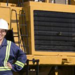 Female miner smiling in front of mining vehicle.