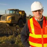 Miner standing in front of a vehicle at a mine site.