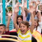 Group of children on a rollercoaster put their hands up and scream.