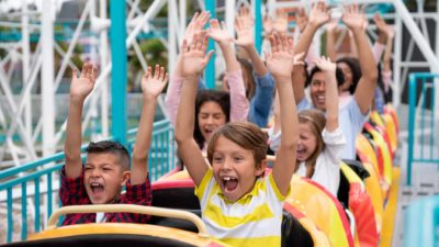 Group of children on a rollercoaster put their hands up and scream.