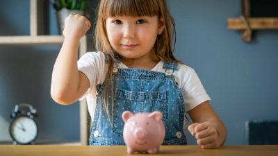 Small girl giving a fist bump with a piggy bank in front of her.