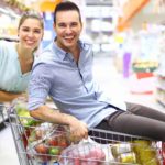 Happy man on a supermarket trolley full of groceries with a woman standing beside him.