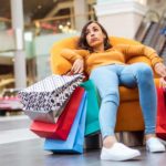 Sad shopper sitting on a sofa with shopping bags.