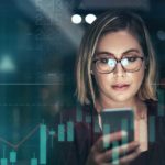 Woman looking at a phone with stock market bars in the background.