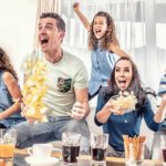 Family jumps up and cheers while watching TV.