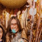 Girls at a party are surrounded by gold streamers, a golden ball and are having a fun time.