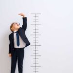 A kid stretches up to reach the top of the ruler drawn on the wall behind.