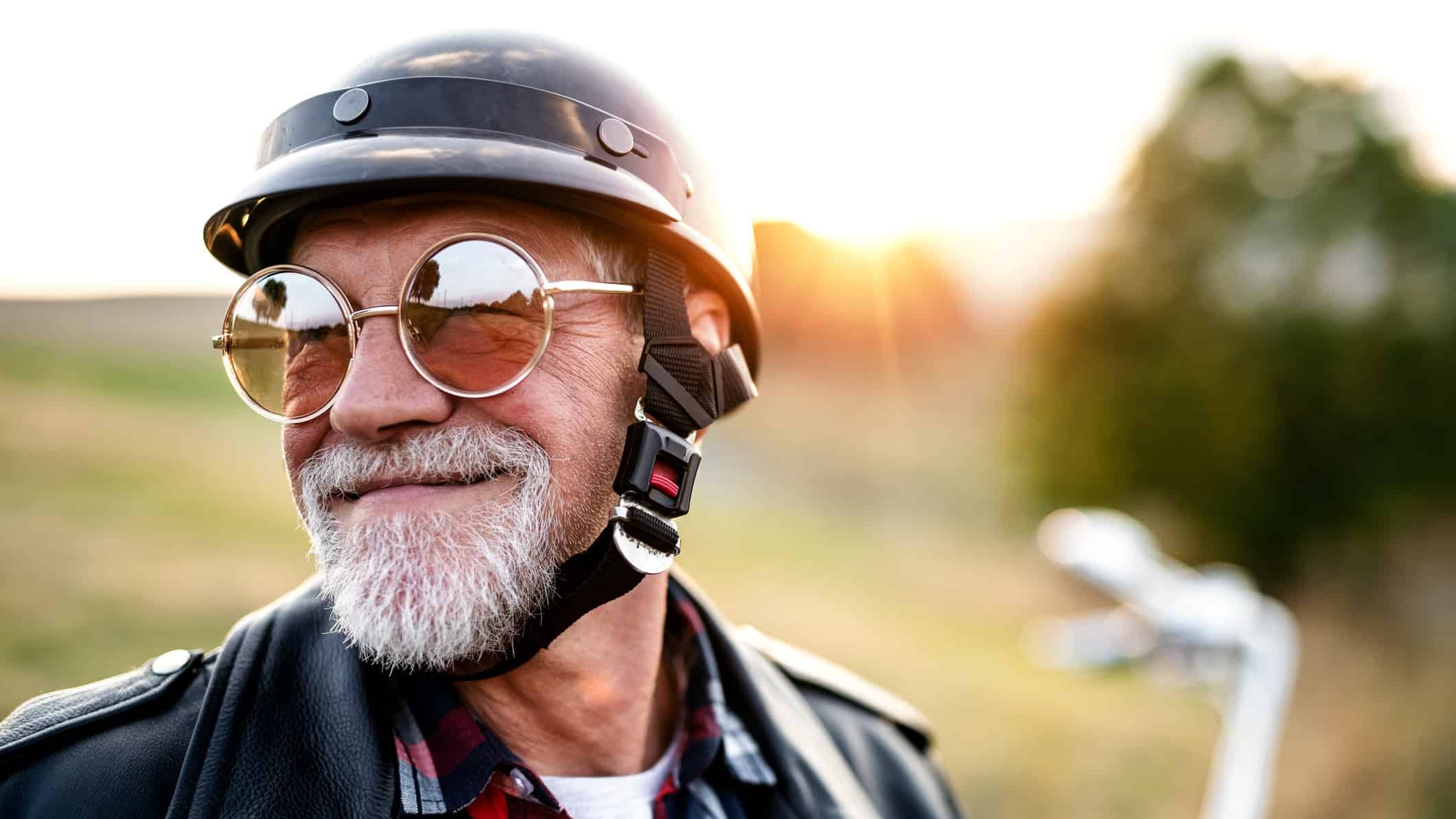 An older man wearing a helmet is set to ride his motorbike into the sunset, making the most of his retirement.