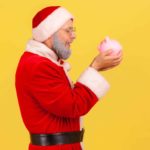 man dressed as santa holding a piggy bank