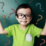 A boy in a green shirt holds up his hands in front of a screen full of question marks.