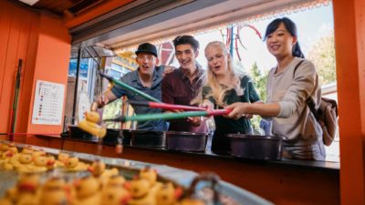 A group of four people plays hook-a-duck at the fairground.